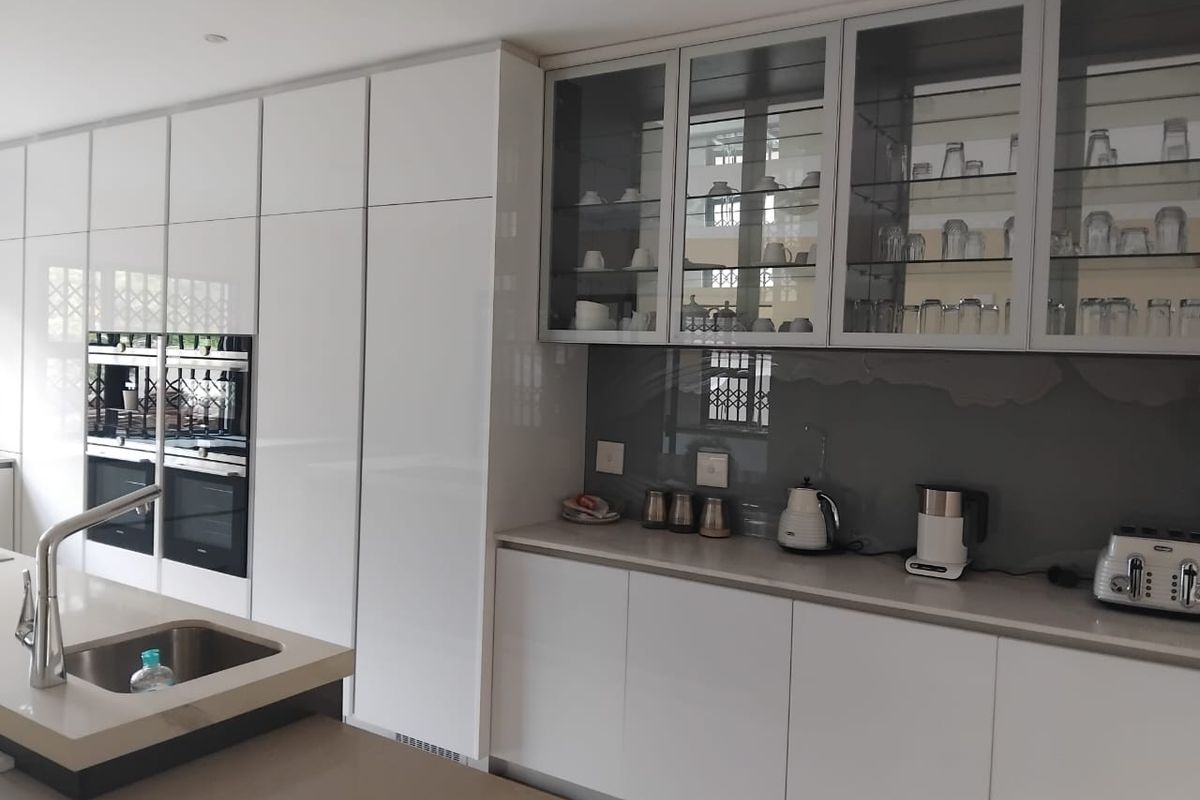Modern kitchen featuring high-gloss white cabinetry, integrated double ovens, a central island with an undermount sink, and sleek stone countertops.