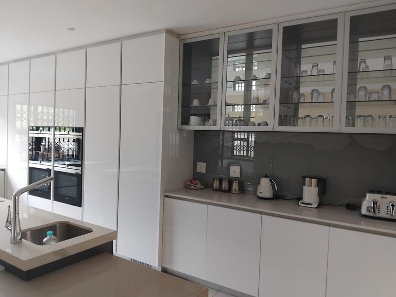Modern kitchen featuring high-gloss white cabinetry, integrated double ovens, a central island with an undermount sink, and sleek stone countertops.