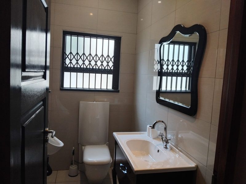 A clean, modern bathroom featuring tiled walls, a vanity basin with chrome mixer tap, and a wall-mounted toilet with a security-gated window.