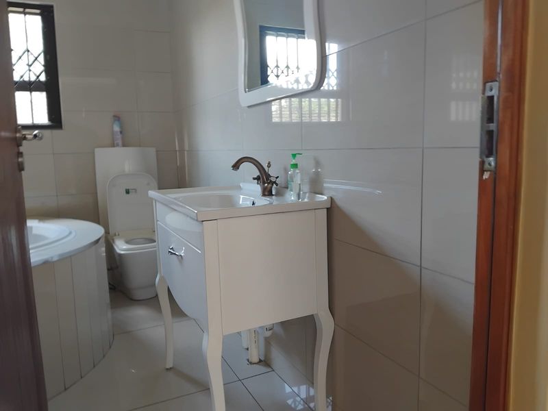 A functional bathroom featuring a white vanity cabinet, basin, toilet, and a bathtub with neutral wall and floor tiling.