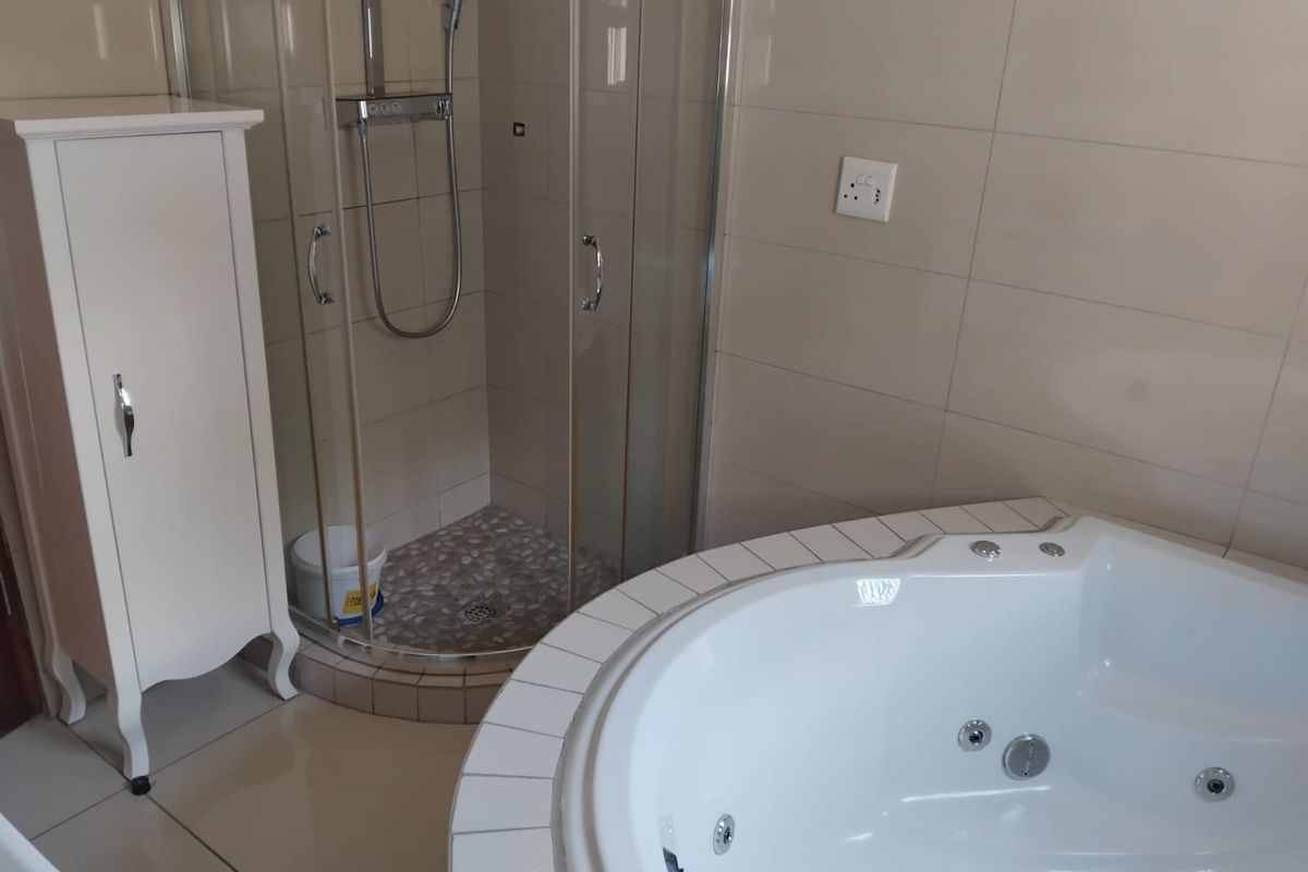 A well-maintained bathroom featuring a corner spa bath and a separate glass-enclosed shower with neutral wall tiling.