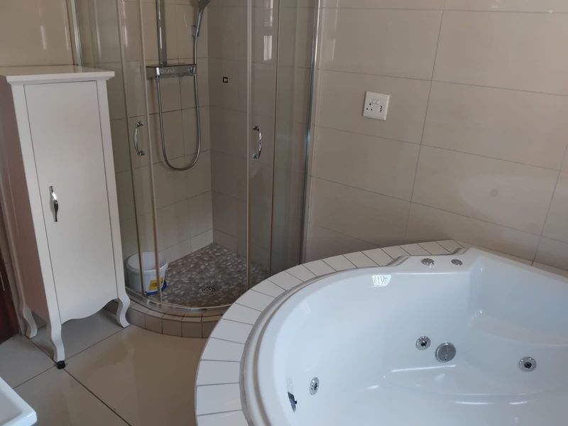 A well-maintained bathroom featuring a corner spa bath and a separate glass-enclosed shower with neutral wall tiling.