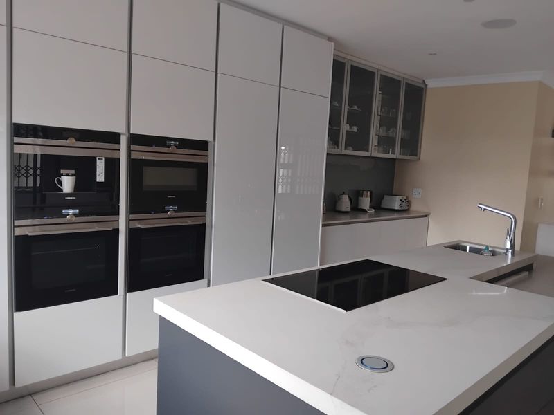 Modern kitchen featuring high-gloss cabinetry, a central island with an induction hob, stone countertops, and integrated high-end appliances.