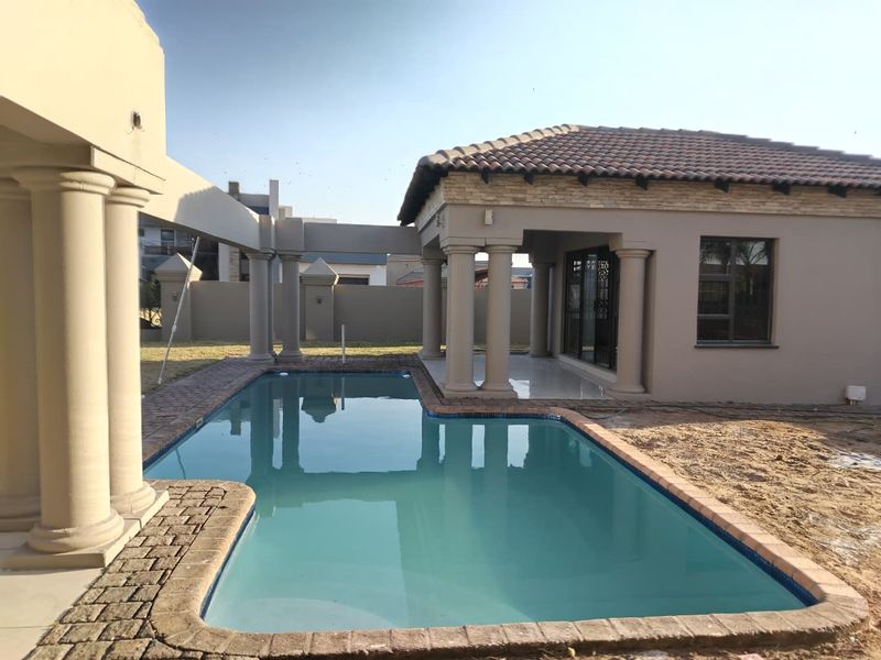 Outdoor pool area featuring a swimming pool, paved surround, and a covered patio structure with classic columns and stone-clad roof detailing.