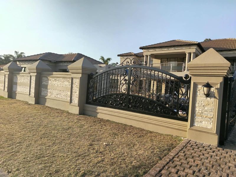 Front view of a luxury residence featuring a decorative wrought iron gate, stone-clad masonry boundary walls, and a multi-level tiled roof structure.