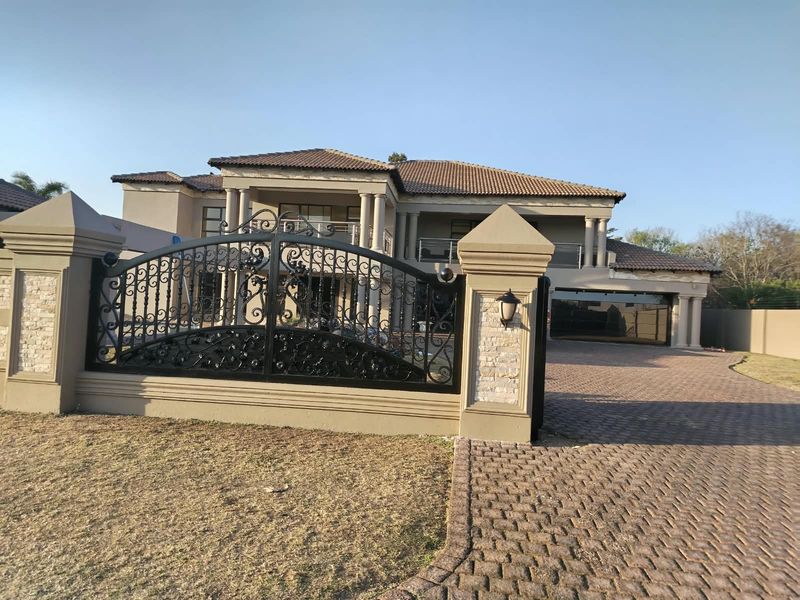 A grand double-story residence featuring a paved driveway, ornate wrought iron gates, stone-clad pillars, and a spacious garage.