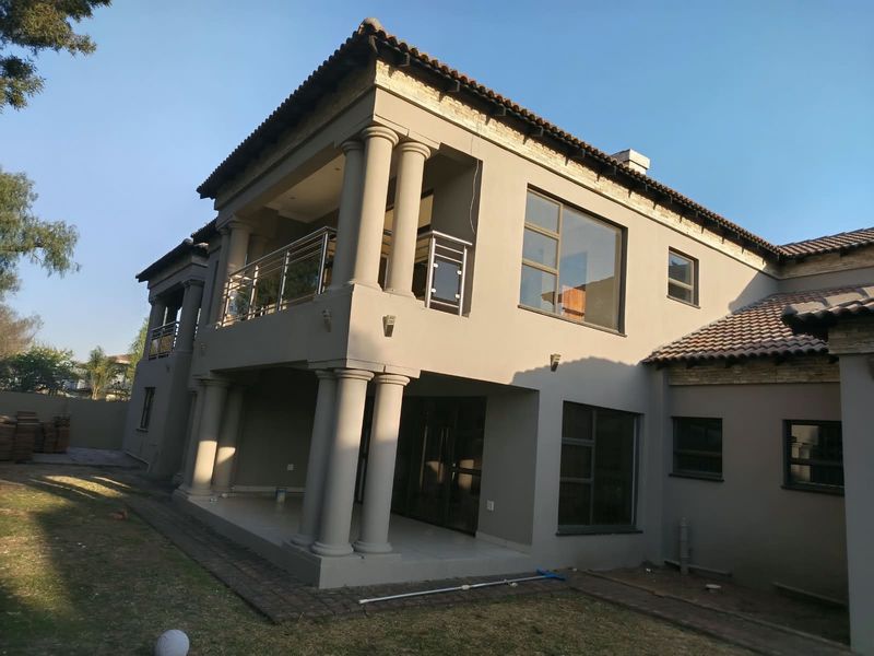 A double-storey rear elevation featuring a covered patio, upper balcony with stainless steel balustrades, and classic architectural columns.