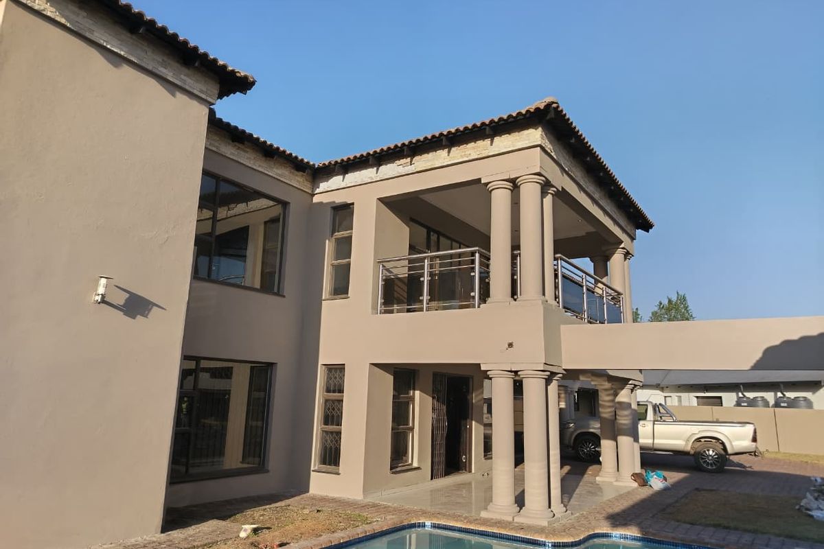 Rear view of a multi-story residence featuring a swimming pool, covered patio, upper-level balcony with stainless steel balustrades, and classic architectural columns.