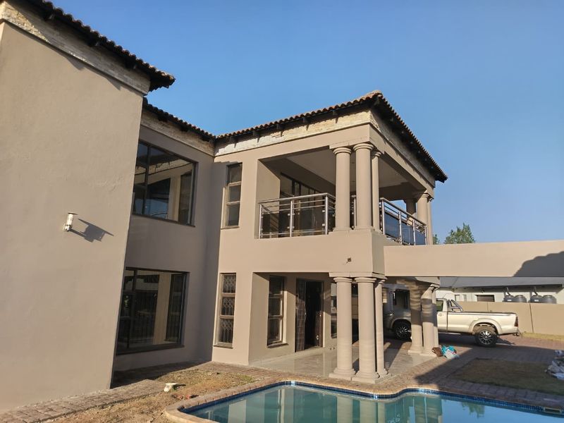 Rear view of a multi-story residence featuring a swimming pool, covered patio, upper-level balcony with stainless steel balustrades, and classic architectural columns.