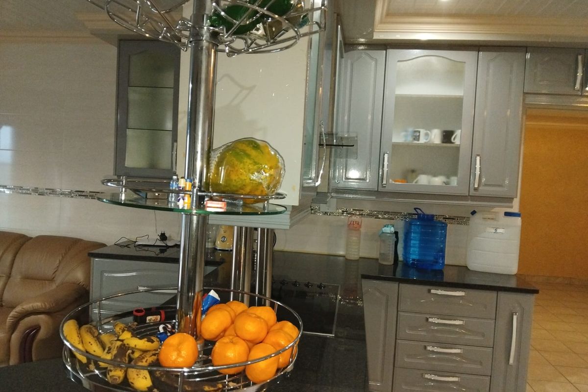 A functional kitchen featuring grey built-in cabinetry, dark granite countertops, and glass-fronted display cabinets with recessed ceiling lighting.