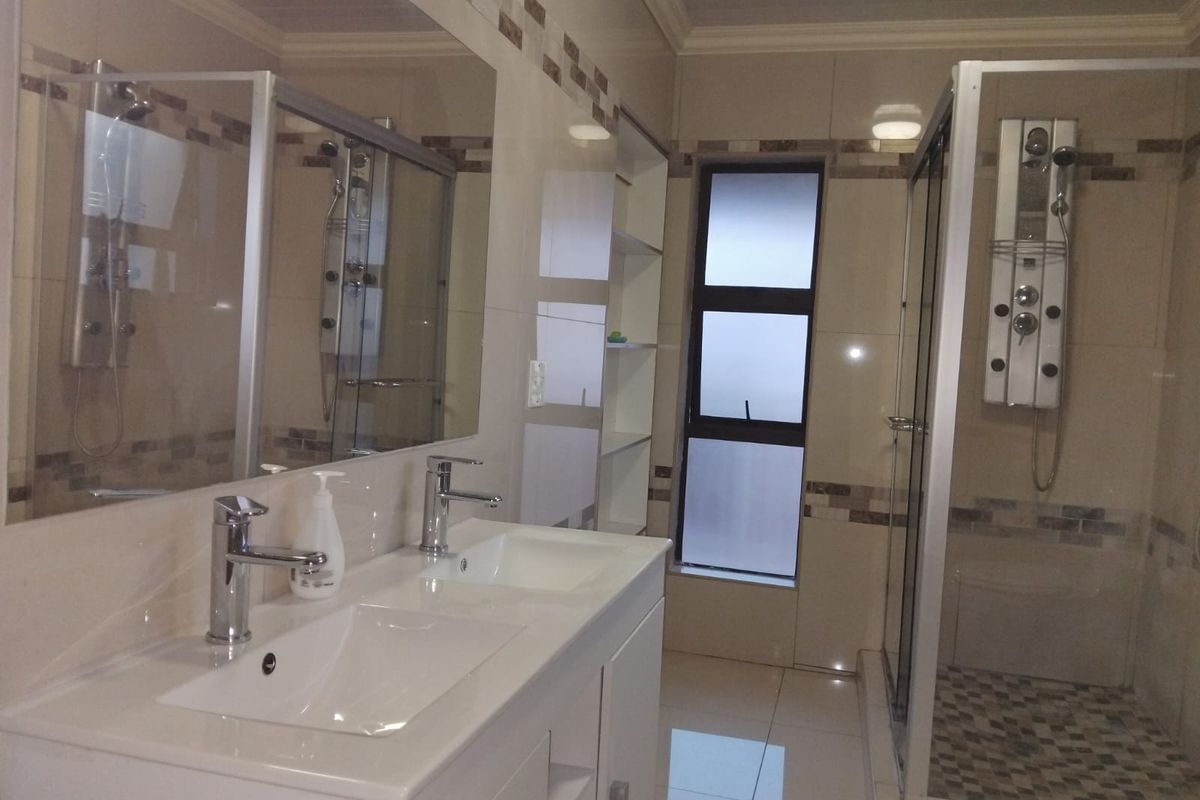 Modern bathroom featuring a double vanity with chrome faucets, a spacious shower enclosure with a multi-jet shower panel, and neutral wall tiling.