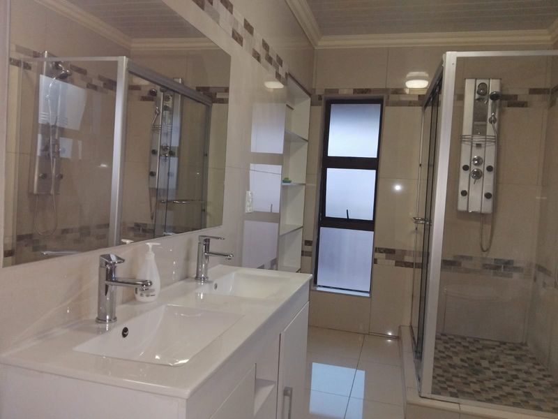 Modern bathroom featuring a double vanity with chrome faucets, a spacious shower enclosure with a multi-jet shower panel, and neutral wall tiling.