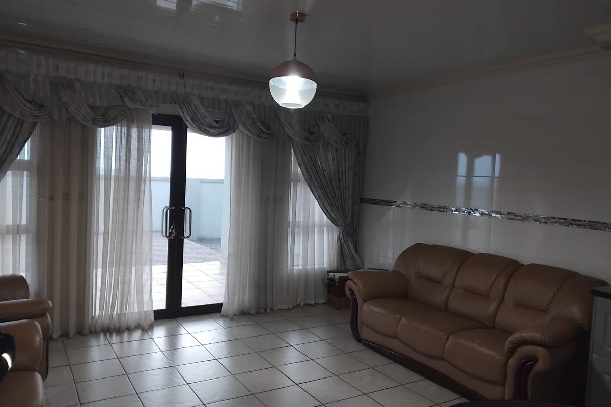 A living room featuring tiled flooring, glossy wall tiles, and a sliding glass door providing access to an outdoor patio area.