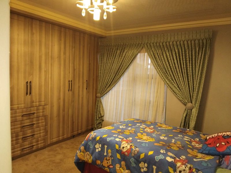 A well-maintained bedroom featuring extensive floor-to-ceiling built-in wooden cupboards, crown molding, and a central ceiling light fixture.