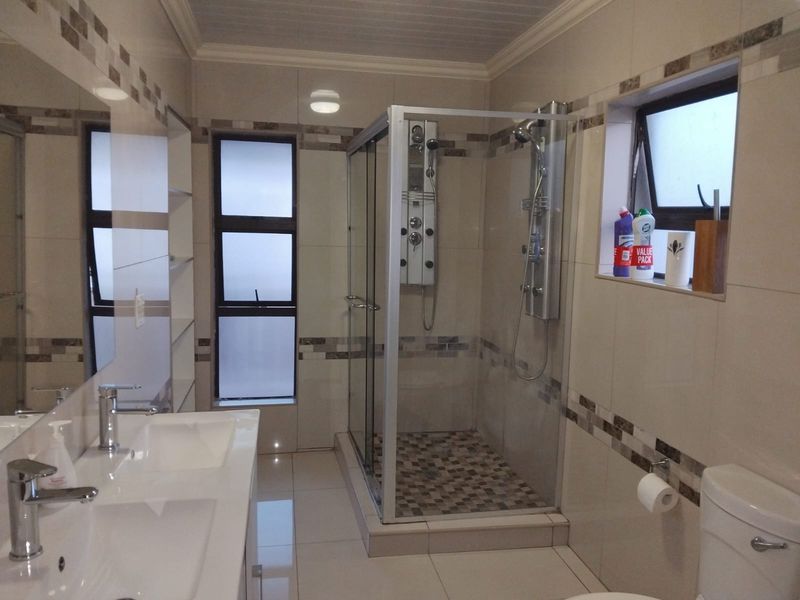 Modern bathroom featuring a double vanity, a spacious glass-enclosed shower with a multi-jet panel, and neutral wall and floor tiling.