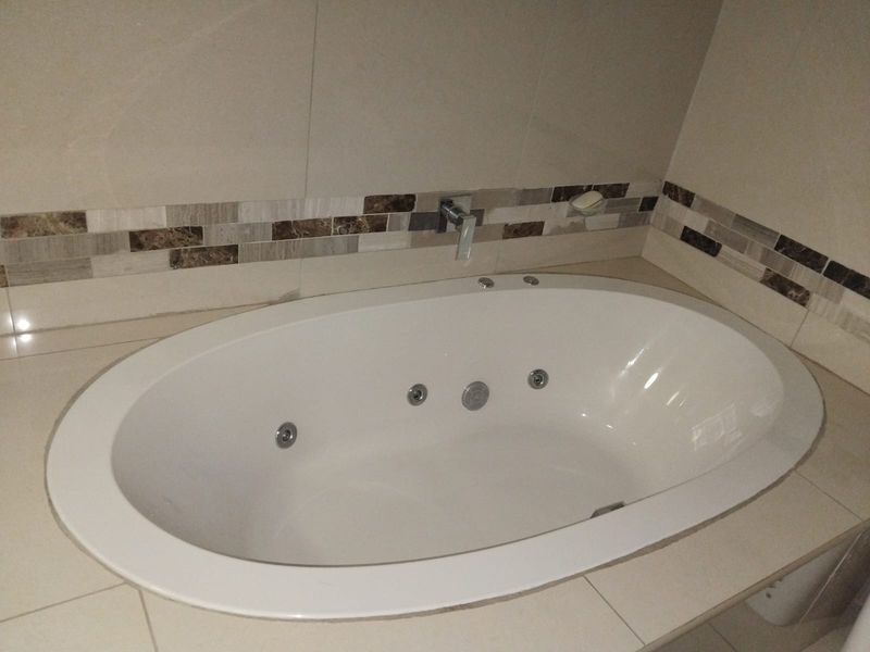 A clean, built-in oval bathtub featuring a jet system, wall-mounted faucet, and neutral tiled surround with a decorative mosaic accent border.