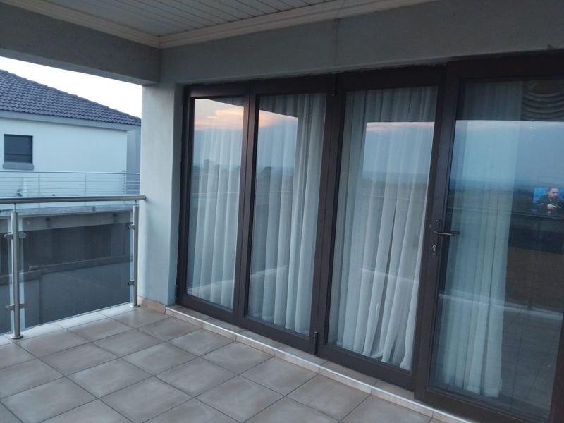 A covered balcony featuring tiled flooring, a modern glass balustrade with stainless steel railings, and large sliding glass doors providing access to the interior.