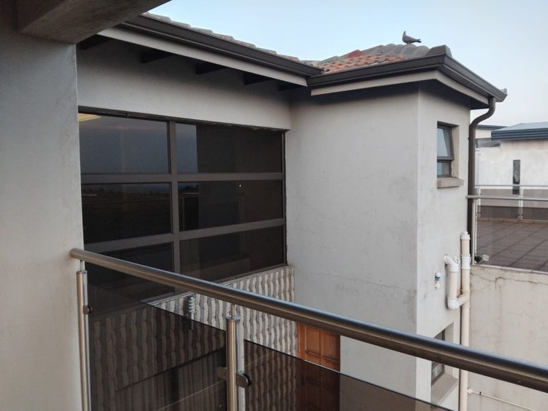 A view from a balcony featuring a modern stainless steel and glass balustrade, overlooking the exterior facade of the property with tiled roofing.