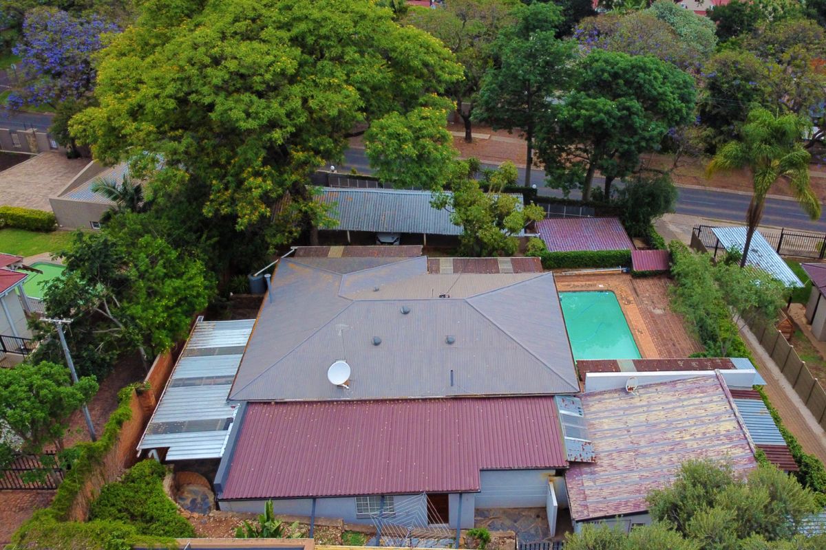 Aerial view of the property showing the main house with a corrugated metal roof, a swimming pool, and surrounding garden area.