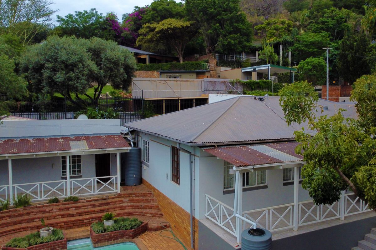 Elevated view of the rear exterior featuring a house with a corrugated metal roof, covered patio areas, brick retaining walls, and a swimming pool.