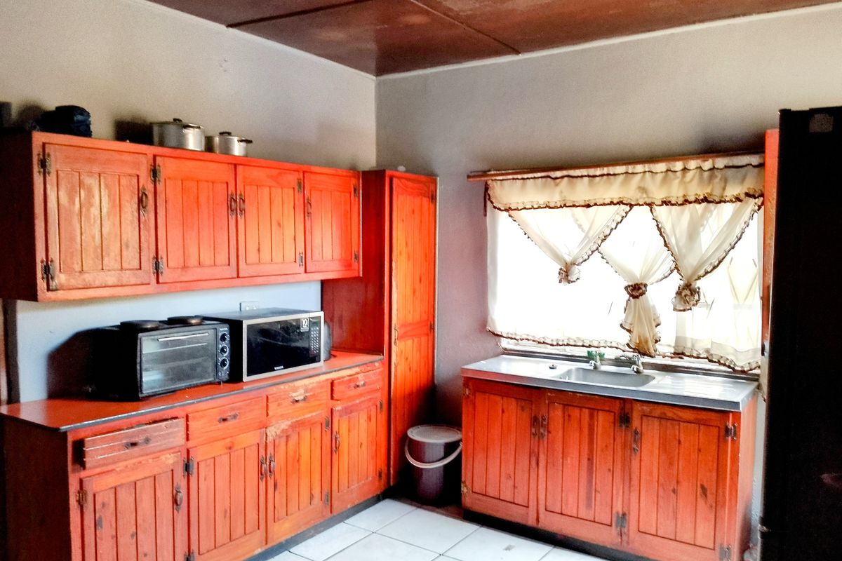 A functional kitchen featuring traditional wooden cabinetry, a stainless steel sink, and tiled flooring, offering potential for a modern renovation.