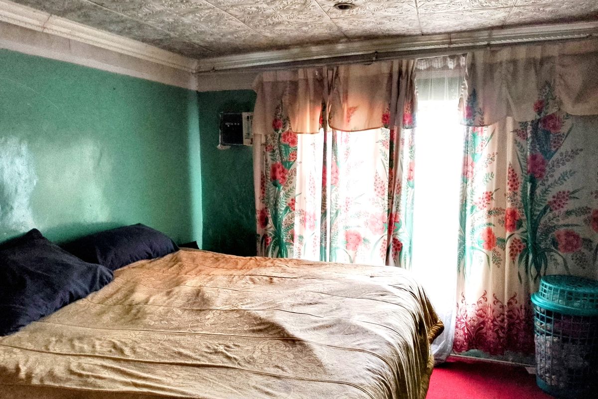 A bedroom featuring textured ceiling tiles and a wall-mounted air conditioning unit, requiring cosmetic updates to modernize the space.