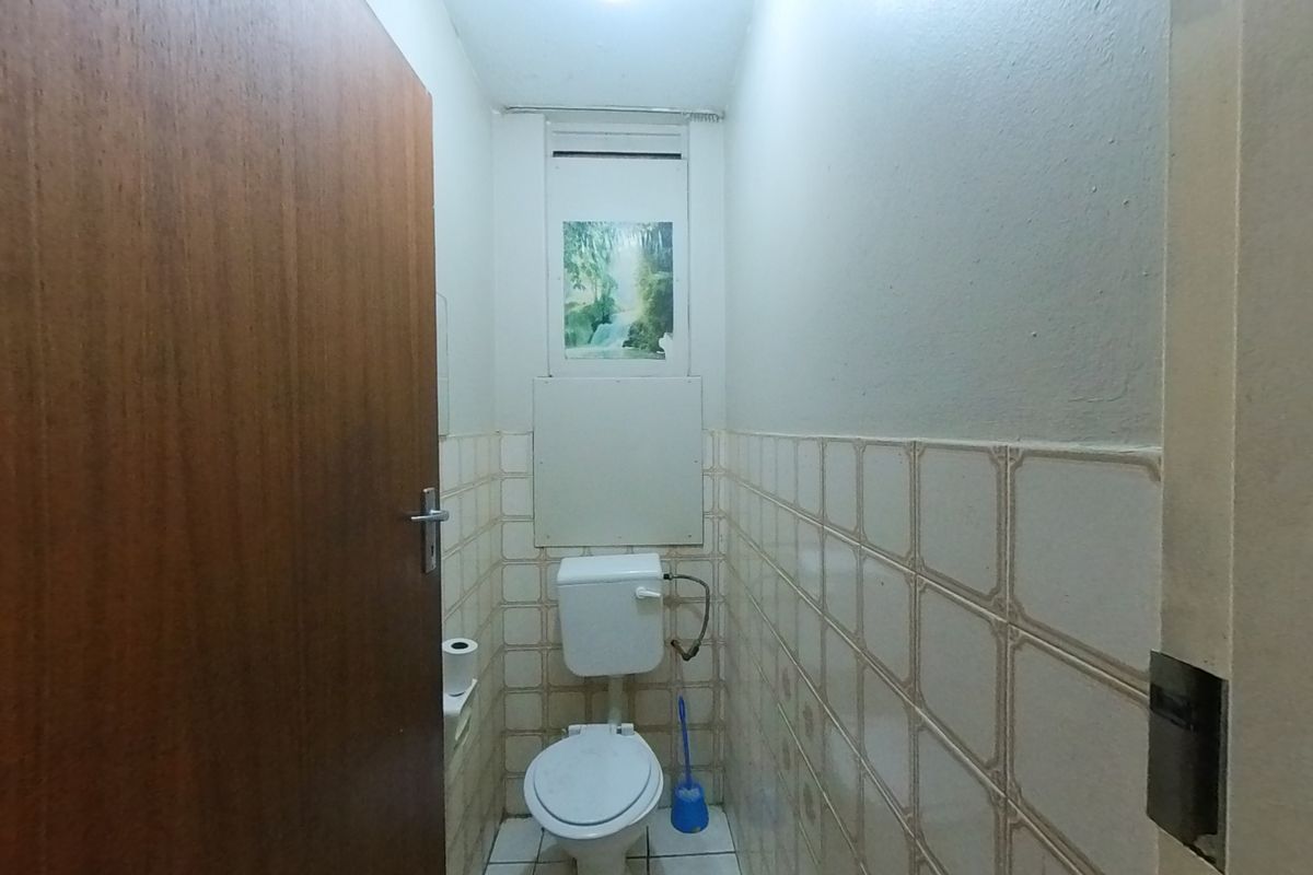 A compact, functional bathroom featuring a standard toilet, tiled walls, and tiled flooring, currently presenting in a dated condition.