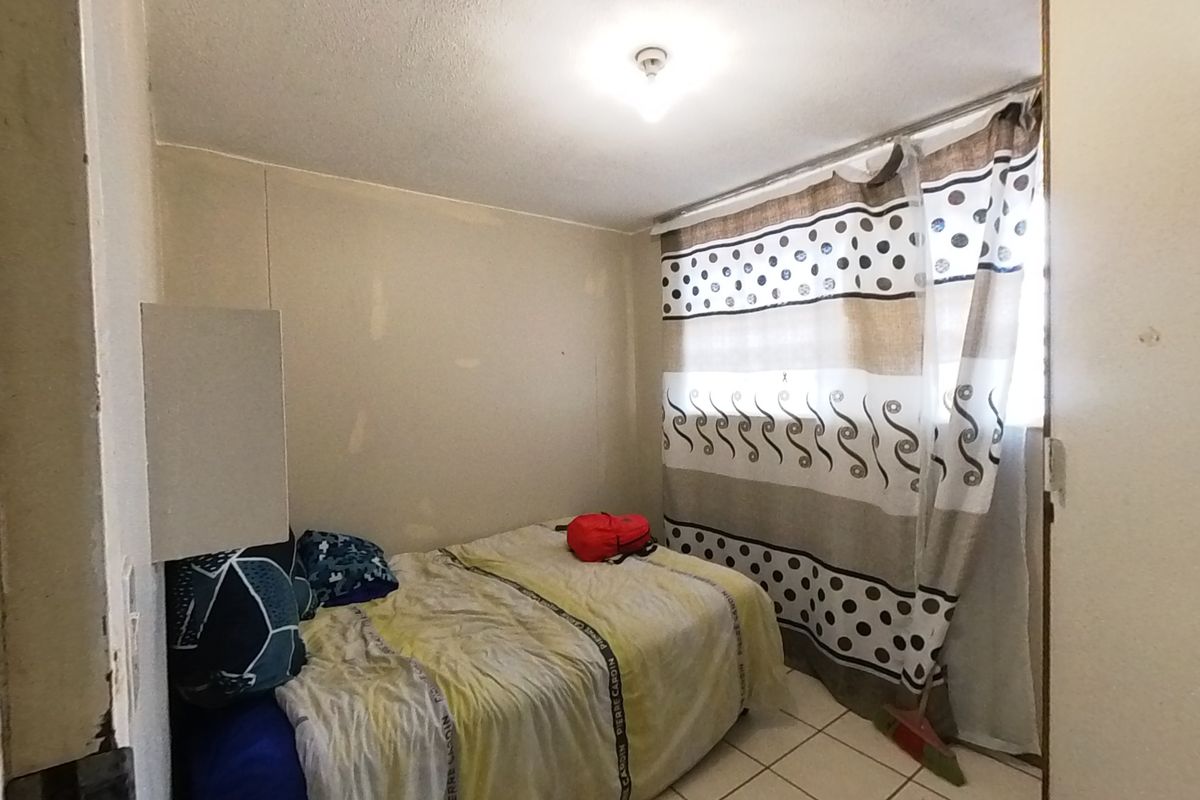 A compact bedroom featuring tiled flooring and a standard ceiling light fixture, currently requiring cosmetic wall repairs and updates.