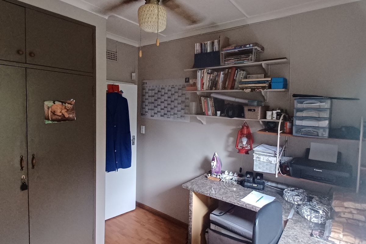 A bedroom featuring a built-in wardrobe, laminate flooring, and a built-in desk, with visible ceiling staining around the fan fixture.