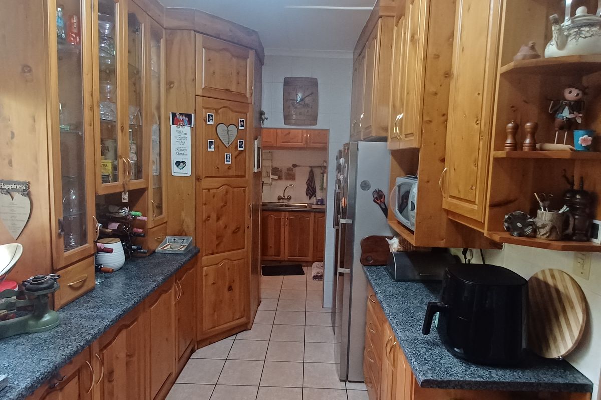 A functional kitchen featuring extensive timber cabinetry, laminate countertops, and tiled flooring, offering a traditional layout with a separate scullery area.