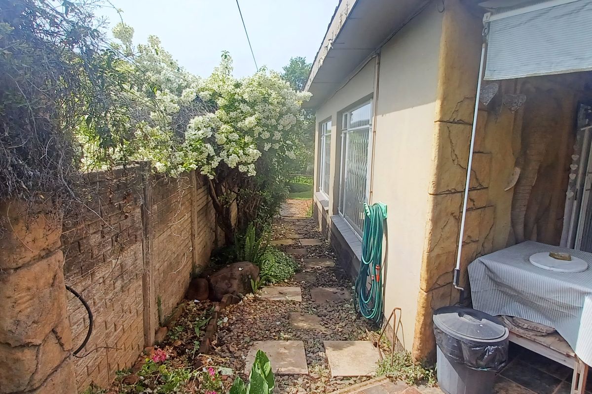 A side garden pathway featuring a stone-effect wall finish, paved stepping stones, and a covered patio area with tiled flooring.
