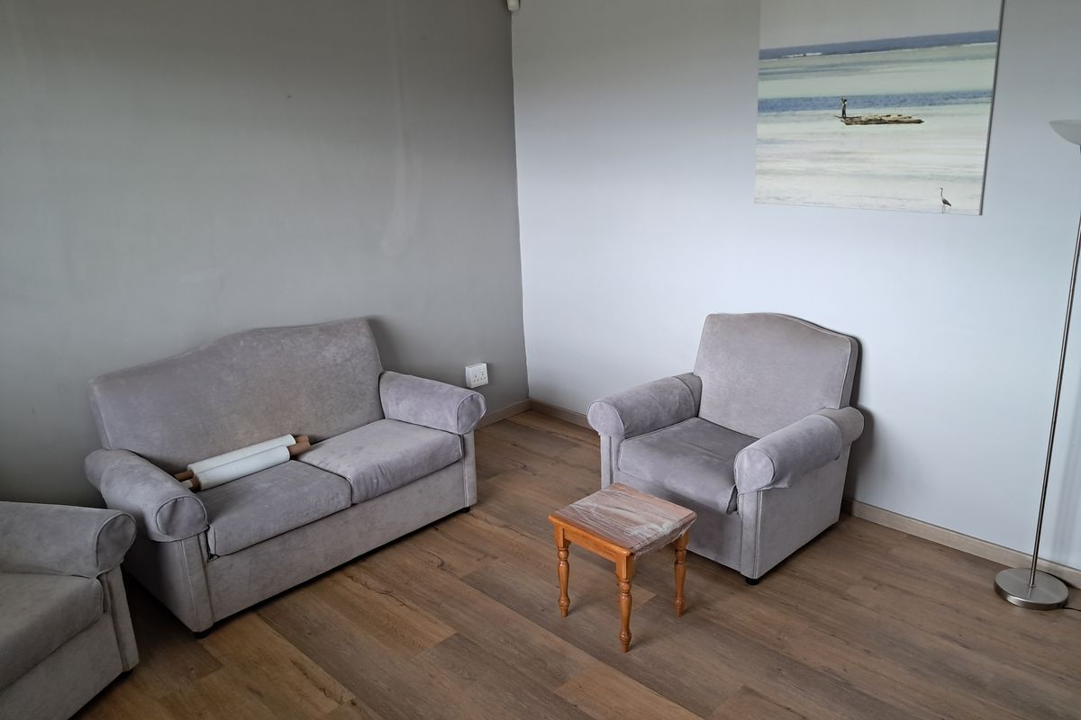 A simple living room area featuring light-toned laminate flooring and neutral grey walls.