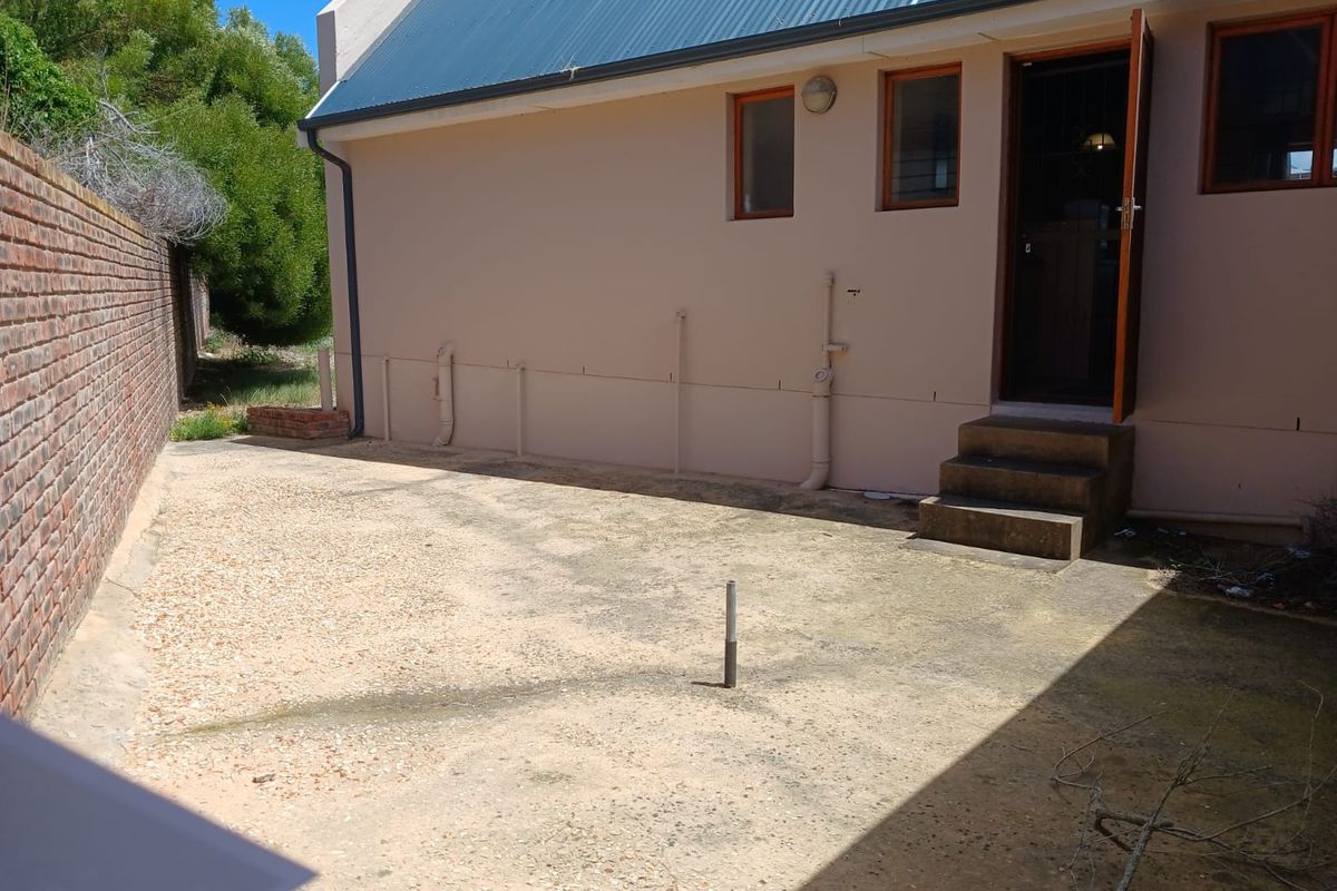 A rear exterior view of the property featuring a concrete paved courtyard, brick boundary wall, and access steps leading to the building entrance.