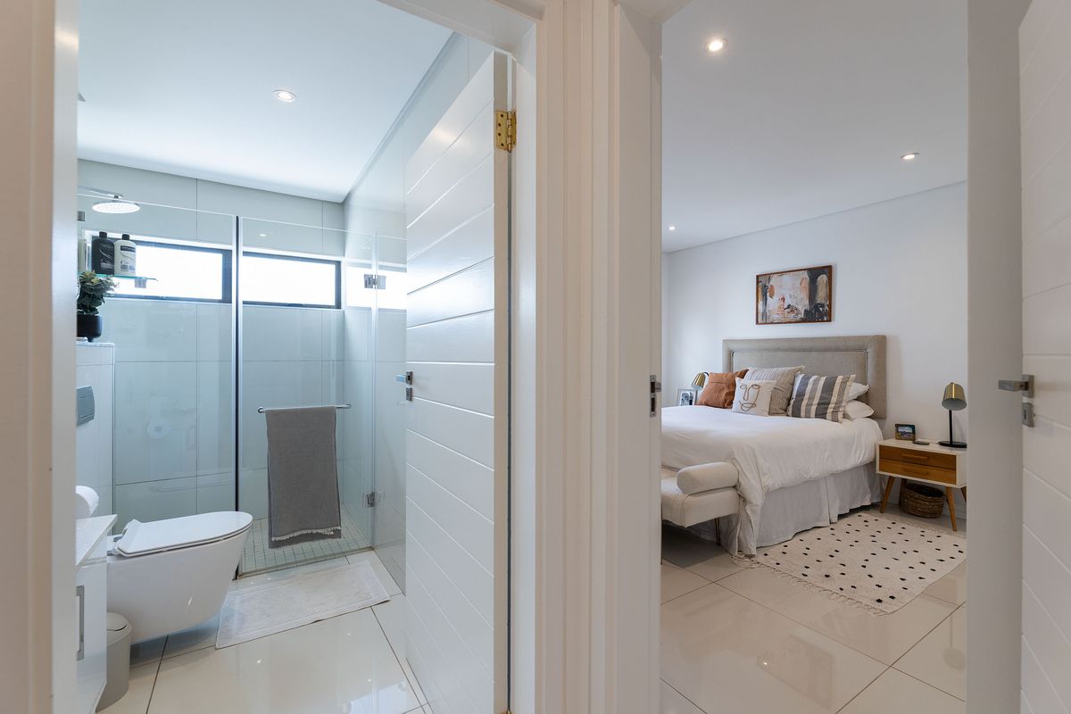 A modern bedroom featuring tiled flooring and recessed lighting, with an adjacent en-suite bathroom equipped with a glass shower and wall-hung toilet.