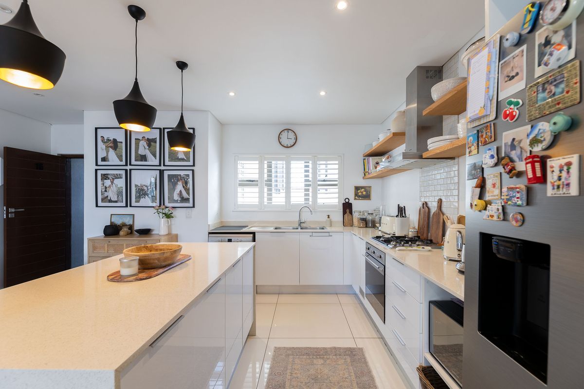 Modern kitchen featuring a central island, quartz countertops, subway tile backsplash, floating timber shelving, and integrated stainless steel appliances.