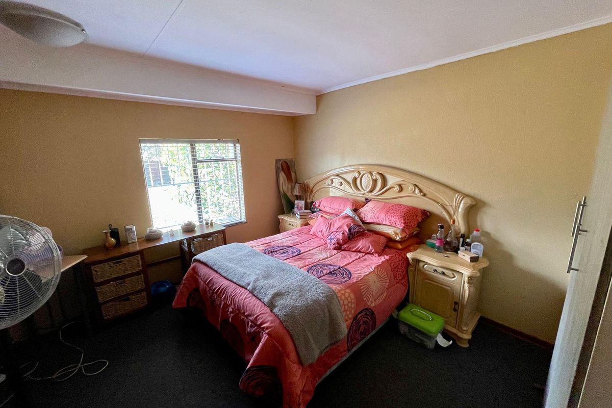 A standard bedroom featuring carpeted flooring, a window with security bars, and a ceiling-mounted light fixture.