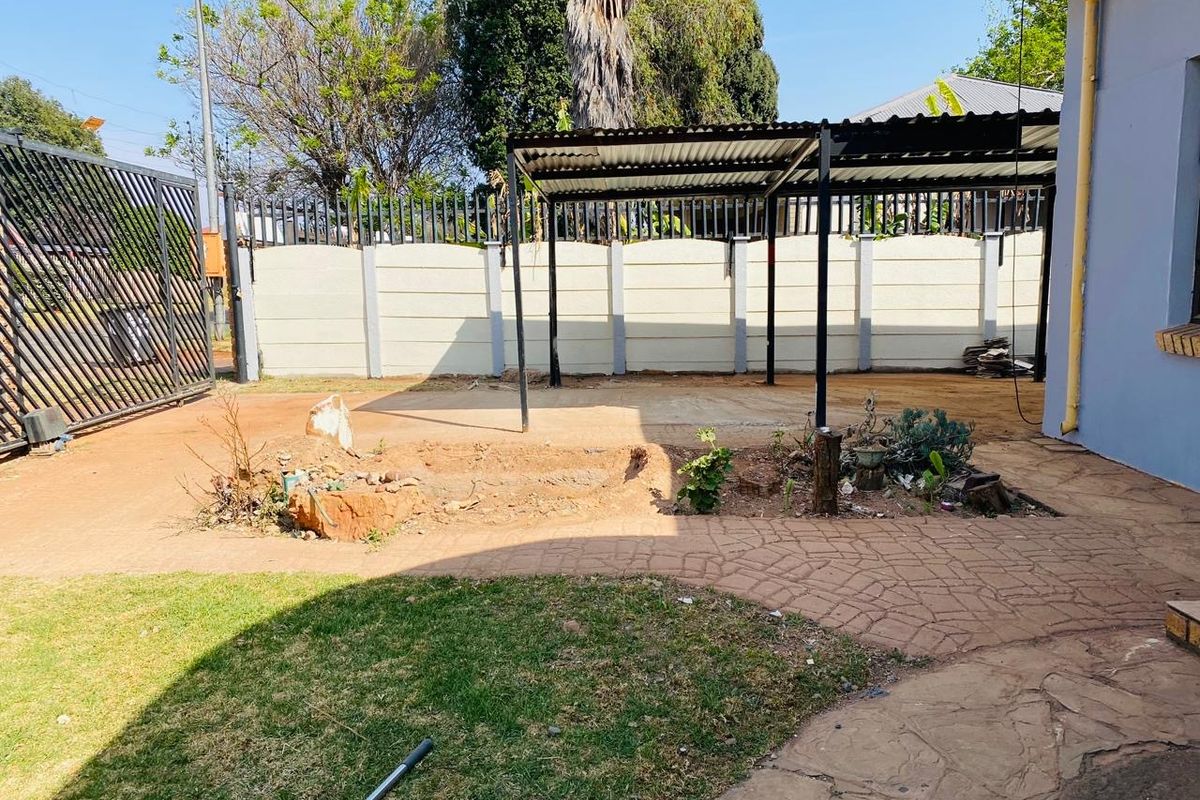 Rear yard area featuring a metal carport, precast boundary wall, paved walkway, and lawn space requiring landscaping.
