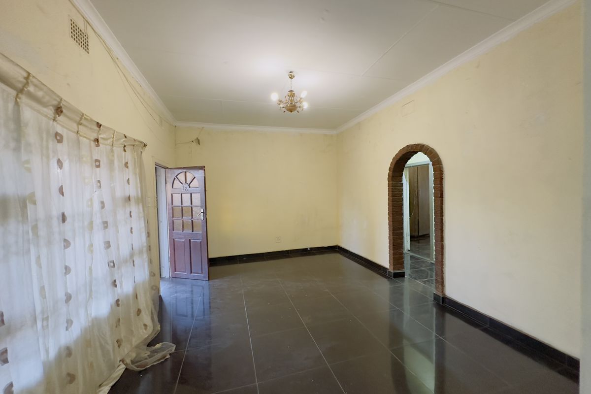 An empty living room featuring dark tiled flooring, a distinctive brick archway, and a timber entrance door, ready for renovation or staging.