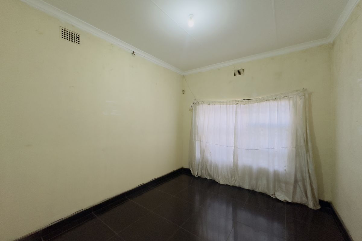 An empty bedroom featuring dark tiled flooring, coving, and wall-mounted air vents, requiring cosmetic updates to the wall finishes.