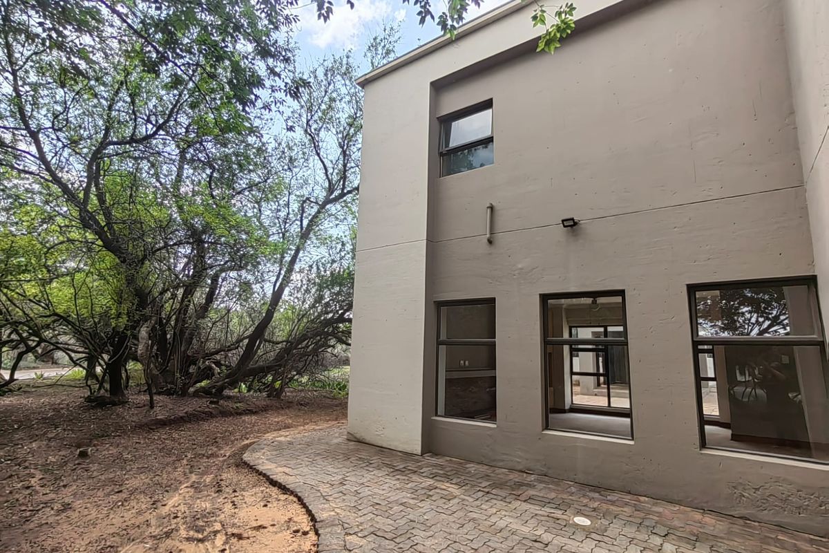 Rear view of the property featuring a paved patio area, modern aluminium window frames, and established garden surroundings.