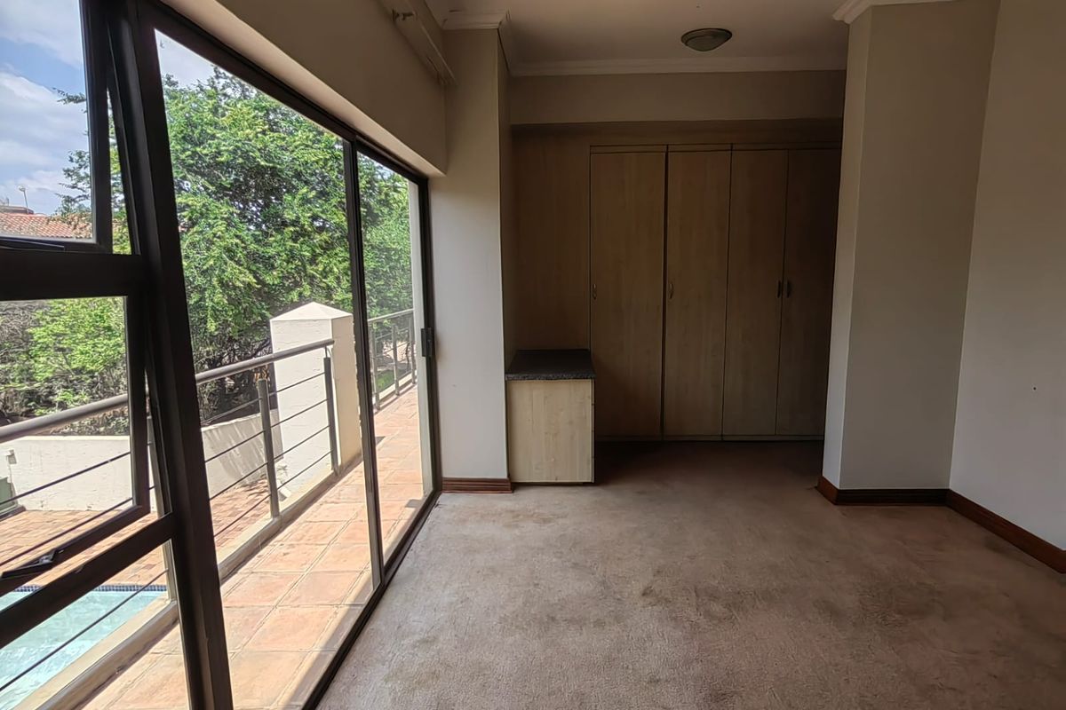 Spacious bedroom featuring built-in cupboards, carpeted flooring, and large sliding glass doors providing access to an outdoor balcony area.