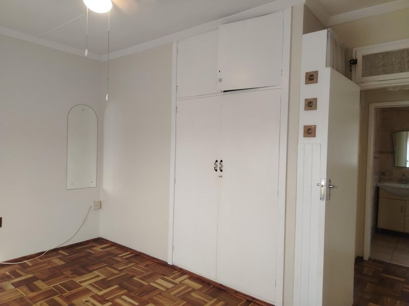A bedroom featuring classic parquet flooring and built-in cupboards, with an adjacent view into a bathroom area.