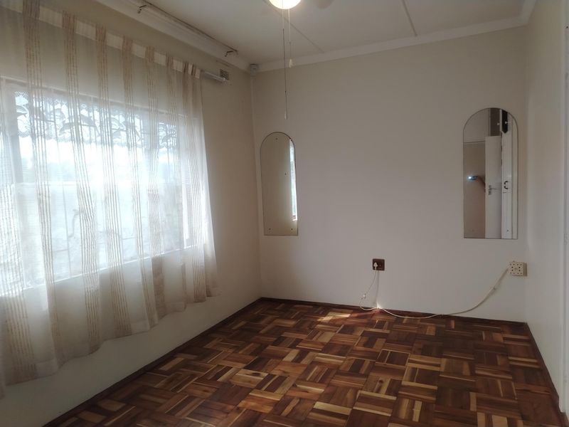 A bright, empty bedroom featuring classic parquet flooring, neutral walls, and two built-in arched wall mirrors.