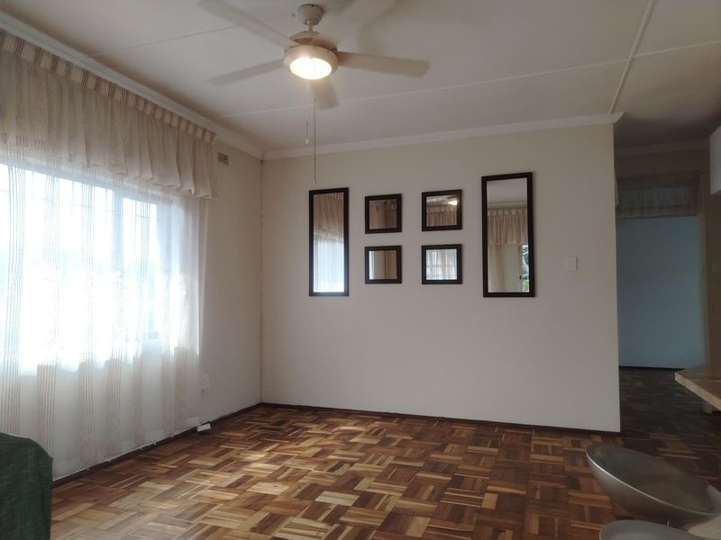 A bright living room featuring well-maintained parquet flooring, a central ceiling fan, and neutral wall finishes, offering a clean and versatile space.