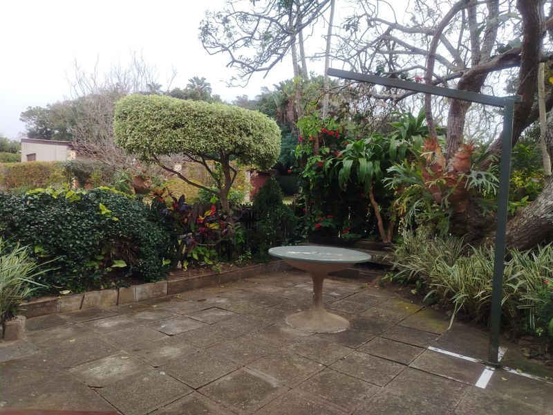 A paved outdoor patio area surrounded by established garden landscaping and mature trees, offering a private space for outdoor relaxation.