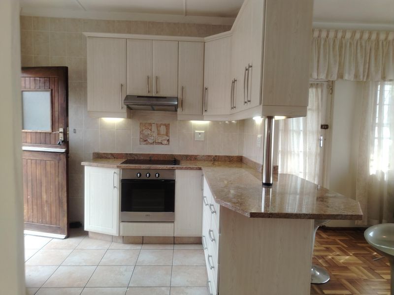 A functional kitchen featuring light-toned cabinetry, granite countertops, a built-in oven and hob, and a breakfast bar, with tiled flooring and backsplash.