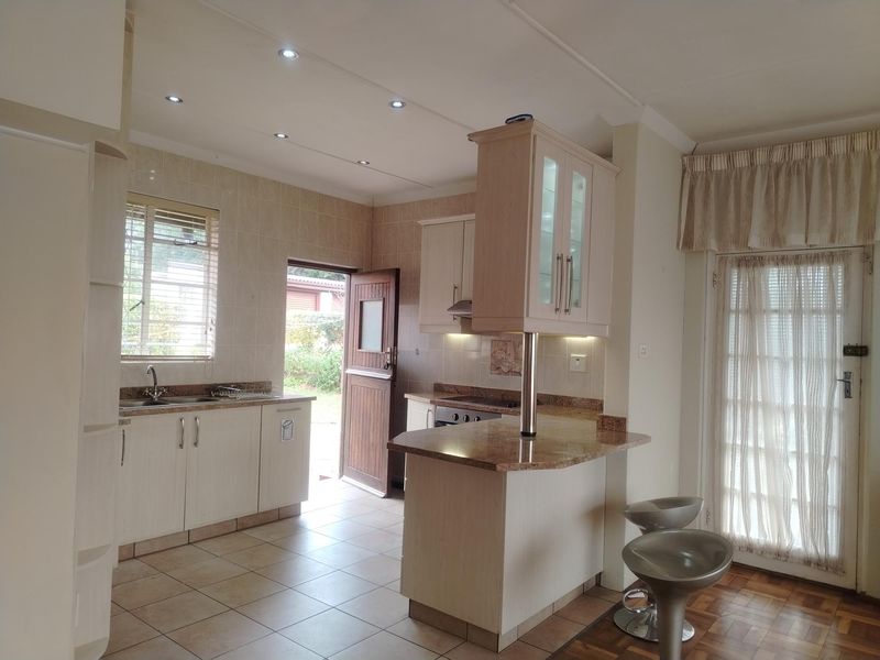 A functional kitchen featuring light-toned cabinetry, granite countertops, built-in appliances, and direct access to the exterior, complemented by recessed lighting and tiled flooring.