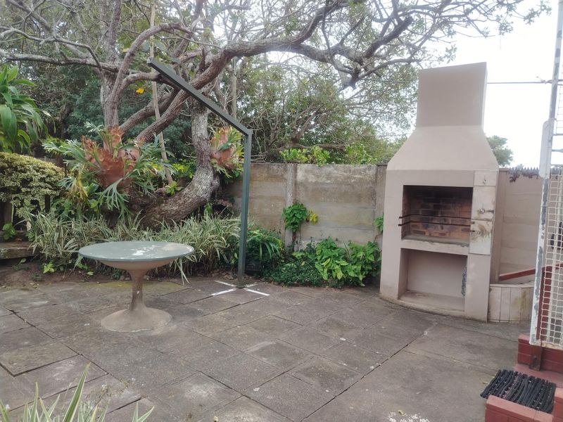 Outdoor patio area featuring a built-in brick braai, paved flooring, and a boundary wall, set within a garden environment.