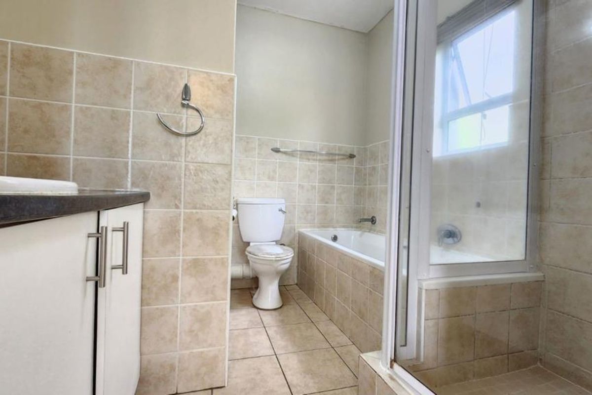 A functional bathroom featuring a vanity cabinet, toilet, bathtub, and a separate shower enclosure with neutral wall and floor tiling.
