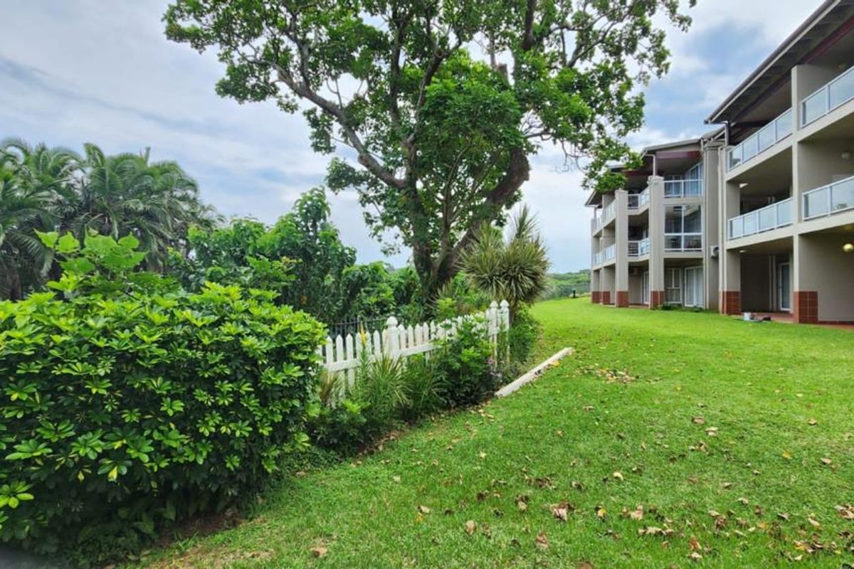 Rear view of the apartment complex featuring a well-maintained lawn, landscaped garden, picket fence, and private balconies with glass balustrades.